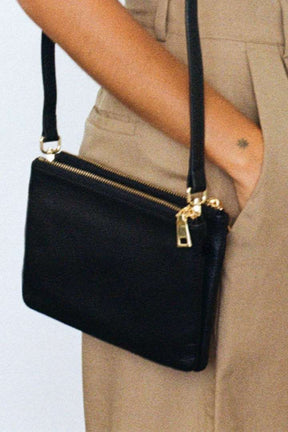 close up pf model wearing MON Purses' double pouch bag in black pebbled leather with gold hardware over her shoulder with the long strap