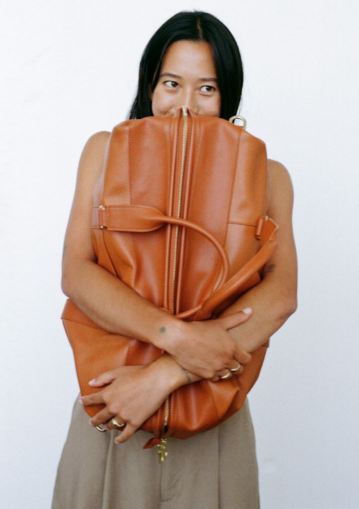 model hugging the mon purse weekender bag in camel brown leather with gold hardware
