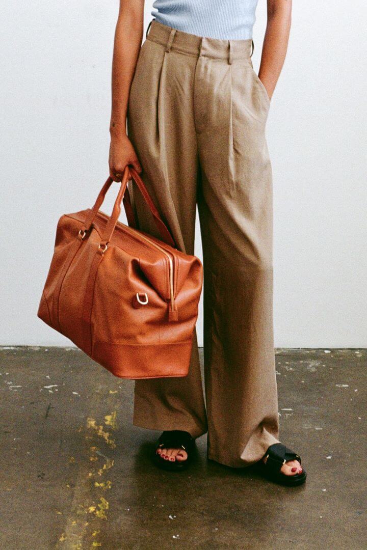 model carrying the mon purse weekender bag in camel brown leather with gold hardware